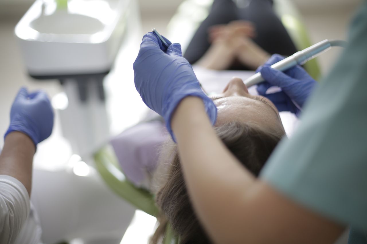 Crop faceless dentist in uniform and gloves using drill and mouth mirror for professional dental treatment in dental clinic
